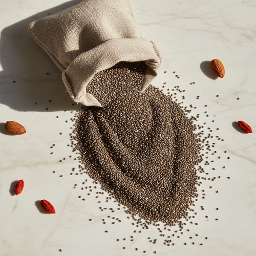 Black chia seeds spilling from a linen bag on white marble, overhead flat lay